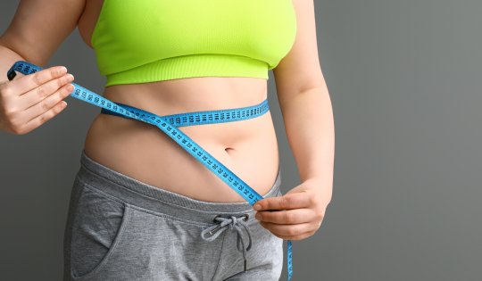 Overweight woman with measuring tape on grey background. Weight loss concept