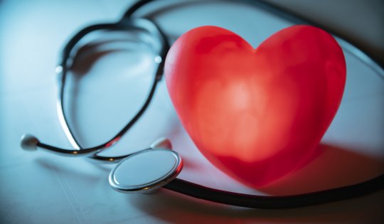 Red heart with stethoscope on blue background. Copy space