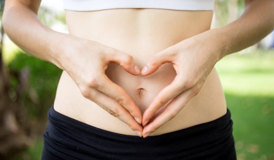 Close-up of female hands shaping heart on belly