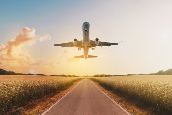 airplane flying above  empty road in rural landscape - travel concept